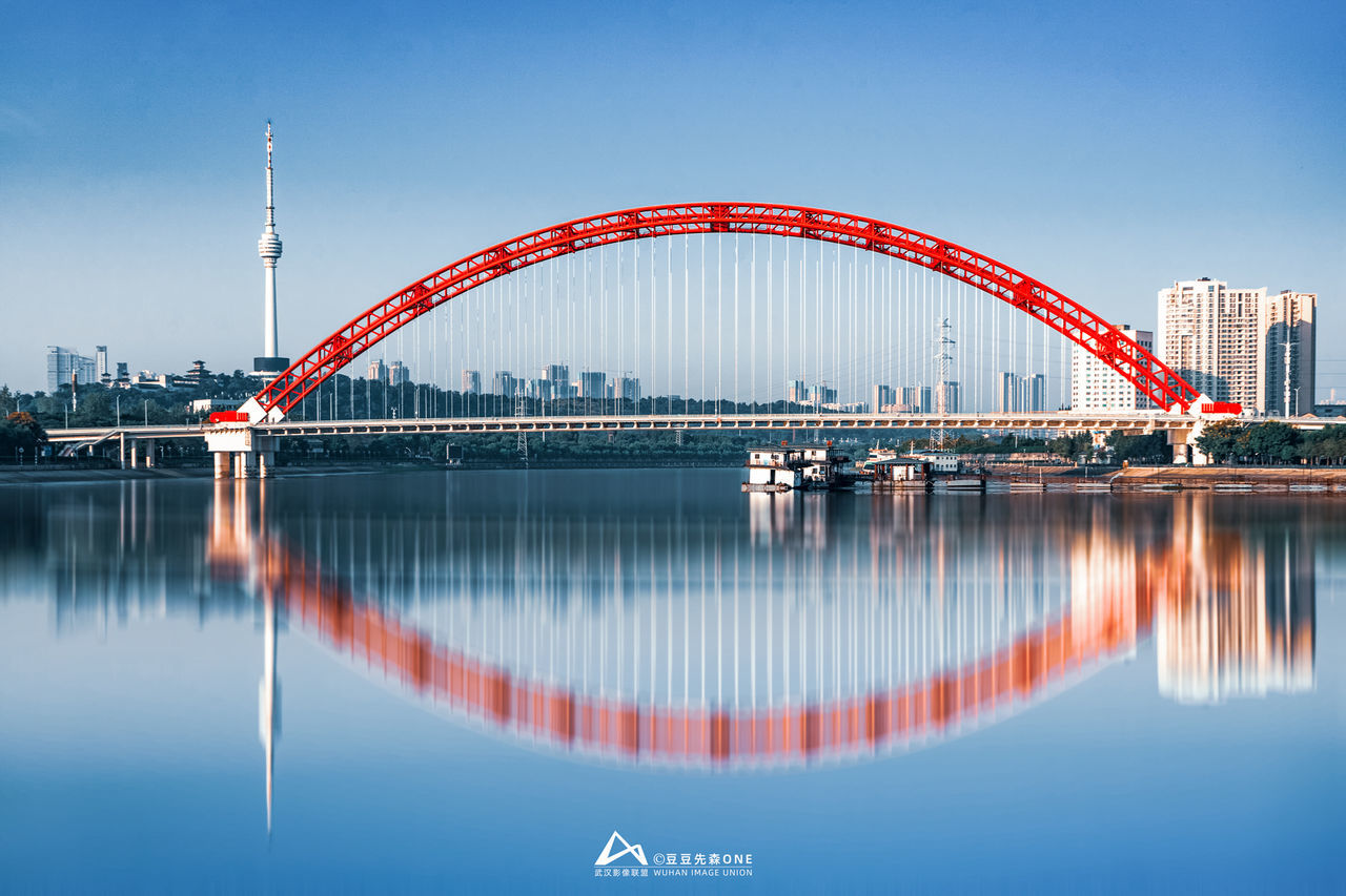 architecture, water, reflection, built structure, bridge, city, travel destinations, sky, nature, landmark, building exterior, transportation, blue, travel, landscape, building, no people, arch bridge, cityscape, harbor, tourism, urban skyline, outdoors, cable-stayed bridge, skyline, red, business, business finance and industry