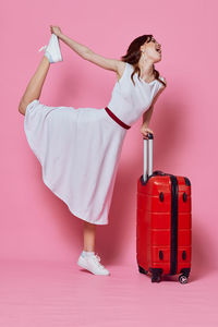 Woman with arms raised standing against pink background