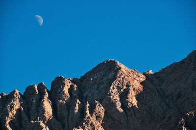 Low angle view of rocky mountains against clear blue sky