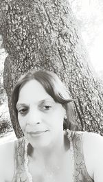 Portrait of smiling young woman against tree trunk