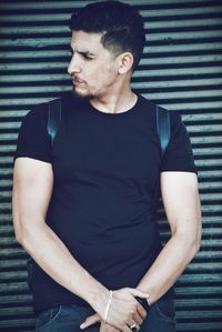 Handsome young man looking away while leaning on closed shutter