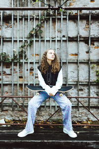 Contemplative girl with skateboard sitting on railing against wall