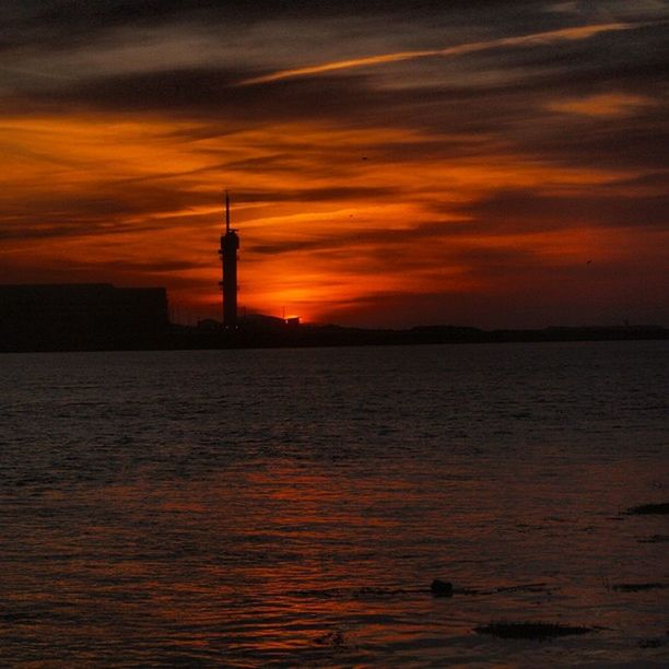 sunset, water, orange color, sky, sea, scenics, silhouette, waterfront, lighthouse, tranquil scene, beauty in nature, tranquility, cloud - sky, built structure, idyllic, nature, architecture, tower, rippled, dramatic sky