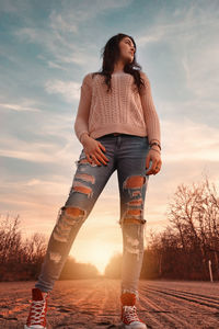 Young woman looking away while standing on land against sky during sunset