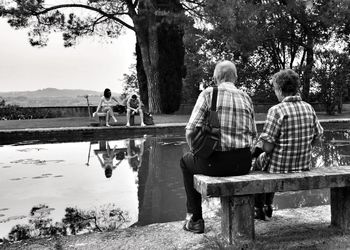 Rear view of couple sitting on lake against trees