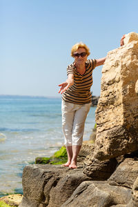 Elderly attractive smiling woman standing on a rock on the seashore