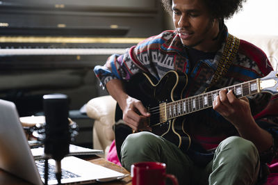 Afro young man learning to play guitar through laptop in living room