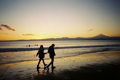 Silhouette couple walking on shore at beach against sky during sunset