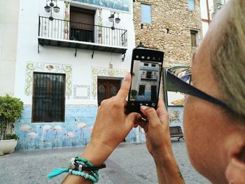 Cropped image of woman photographing building from mobile phone