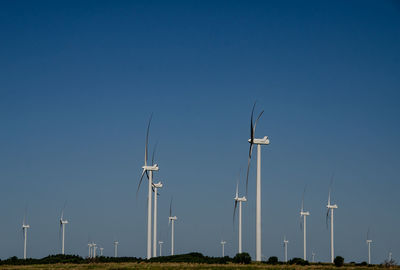 Wind turbines on field against clear blue sky