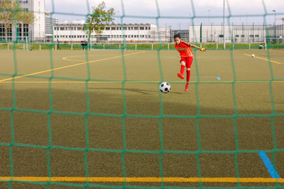 Girl kicking soccer ball into the goal seen behind the net