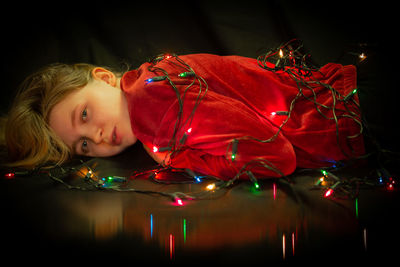Portrait of cute girl lying on illuminated christmas lights