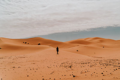 Man on sand dune in desert against sky