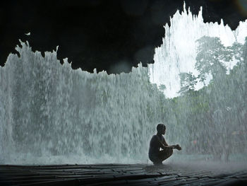 Man sitting by waterfall against sky