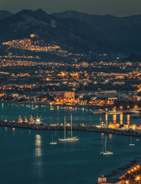 Illuminated city by sea against sky at night