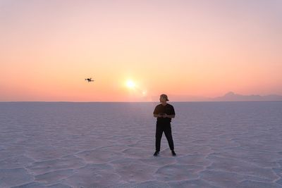 Rear view of woman standing at beach against sky during sunset