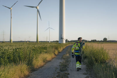 Technician walking on field path at a wind farm with climbing equipment