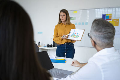 Businesswoman explaining graph to colleagues holding clipboard at office