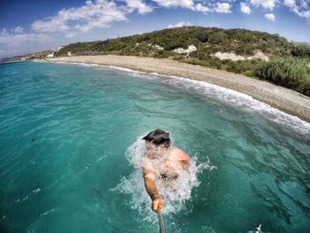 High angle view of man swimming in sea while holding monopod against sky