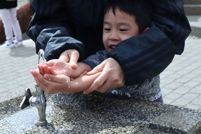 Midsection of man helping boy in drinking water from fountain