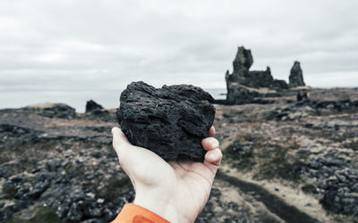 Cropped hand holding basalt rock at snaefellsnes against sky