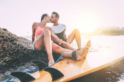  couple holding hands and kissing while sitting on shore of beach