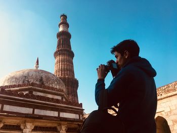 Low angle view of young man photographing mosque against clear blue sky