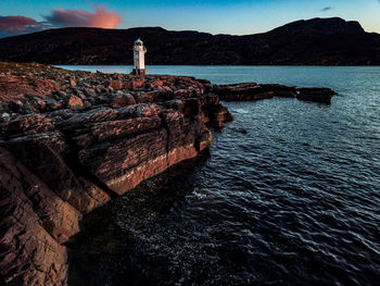 Lighthouse on rock by sea against sky