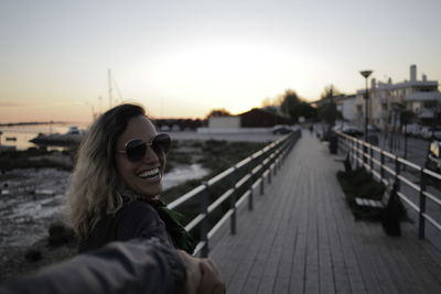 Portrait of smiling woman at harbor against sky during sunset