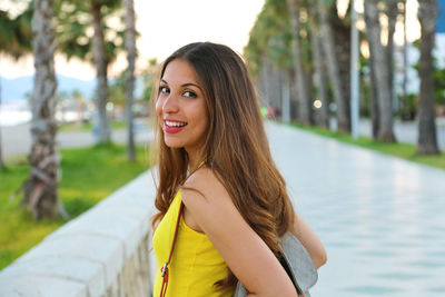 Portrait of smiling young woman standing amidst palm trees