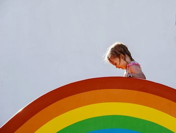 Low angle view of girl on top of rainbow  against sky