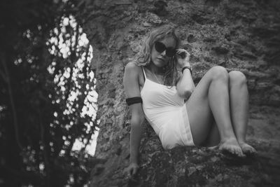 Full length of woman in sunglasses sitting against wall