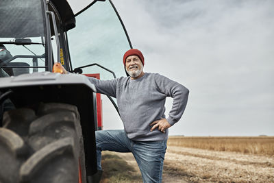Confident farmer standing with hand on hip by tractor at farm