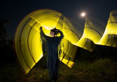Full length of woman with light painting standing against sky at night