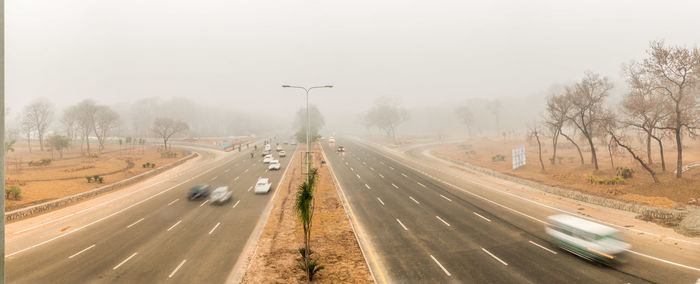 Vehicles on road by trees against sky