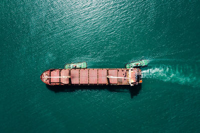 Red oil ship tank and tugboat sailing on green sea photograph aerial from drone point of view