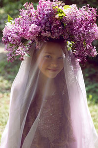 Caucasian girl child seven years old in a purple dress stands in nature with a wreath of lilacs