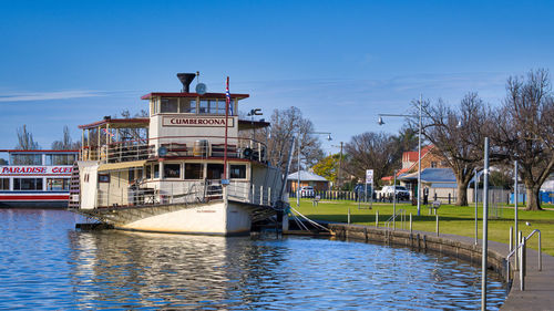 Boats moored in river by buildings against sky