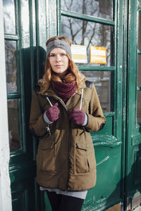 Portrait of beautiful young woman standing by closed door