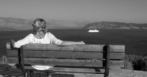 Rear view of woman sitting by sea on bench