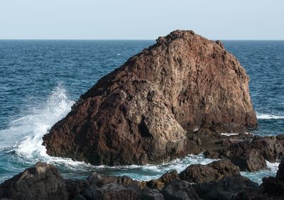 Rock formation in sea against clear sky