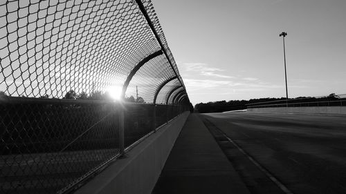 Low angle view of chainlink fence by road against sky on sunny day