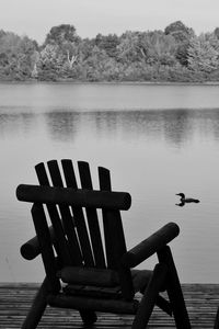 Empty chairs by lake against sky