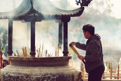 Man holding incense while standing against temple