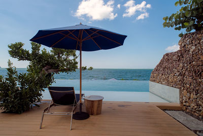 Lounge chairs by swimming pool at beach against sky