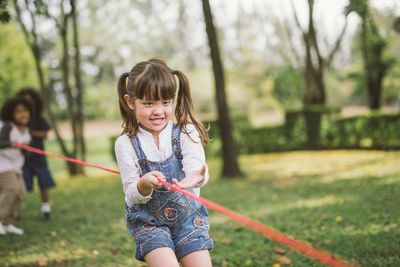 Smiling friends pulling rope while standing at park