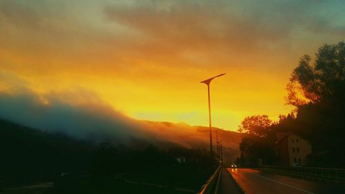 Road by silhouette trees against sky during sunset