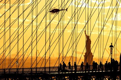 Silhouette of brooklyn bridge against statue of liberty at sunset