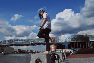 Full length of man skateboarding on bridge in city against sky