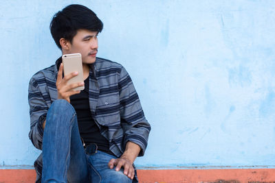 Young man using mobile phone against wall
